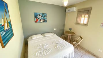 Quarto com cama, uma mesinha redonda, uma cadeira, um quadro e um aparelho de ar condicionado.