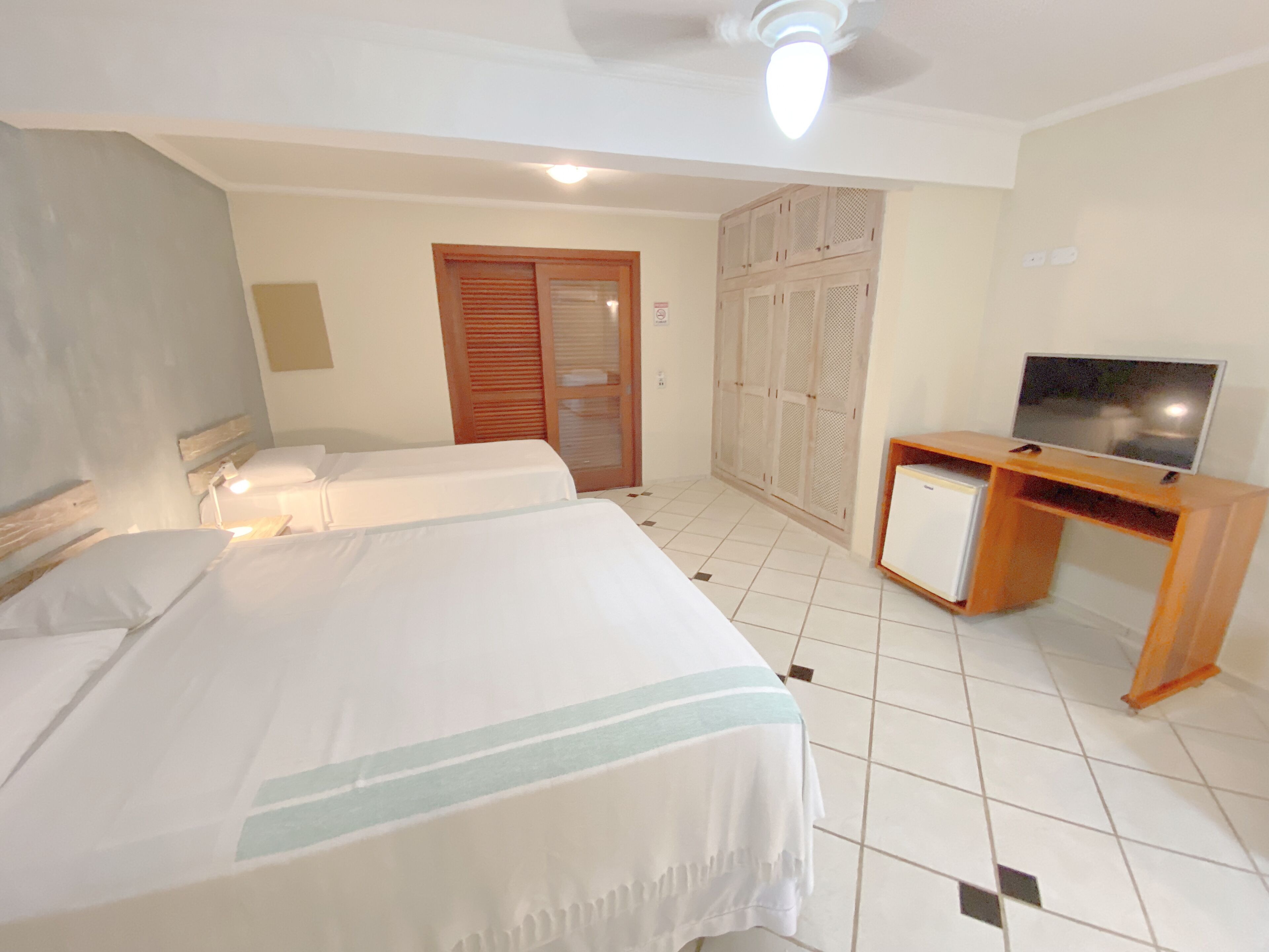 A hotel room with two beds, a TV, a wardrobe, and a desk.