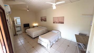 Quarto com duas camas, uma escrivaninha, uma cadeira, ventilador de teto e um quadro na parede.