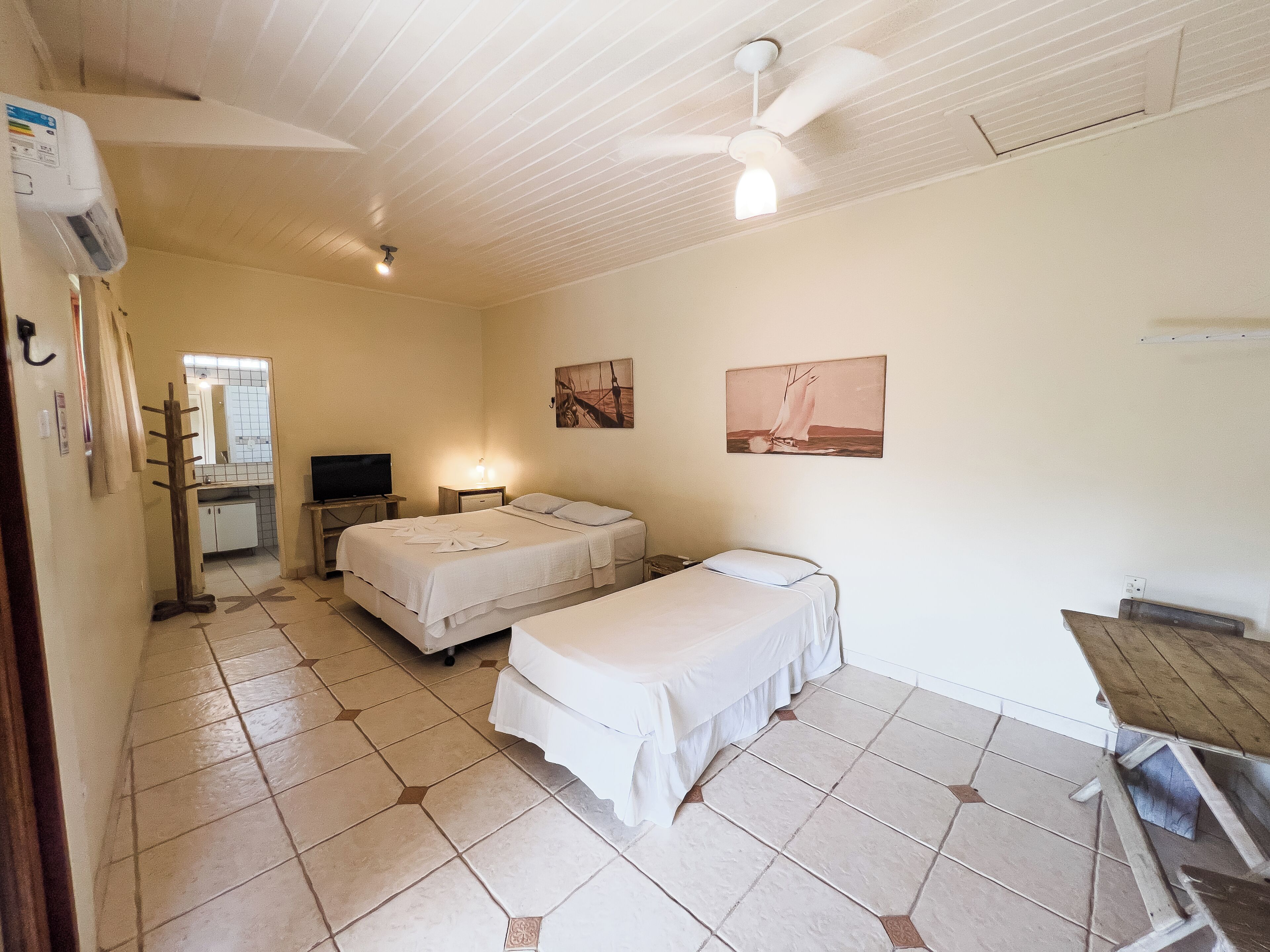 Une chambre d’hôtel avec deux lits, un ventilateur de plafond, une télévision, un bureau et une salle de bain avec un miroir et un lavabo.