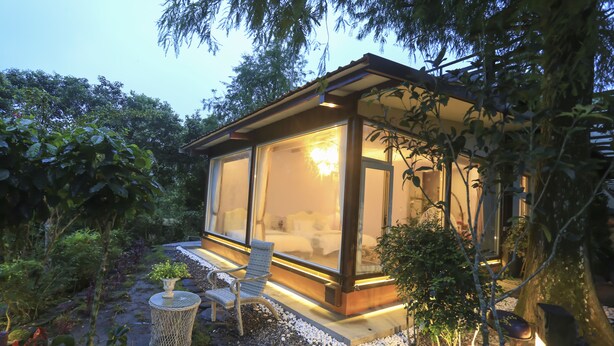 A modern glass house with a wooden deck, surrounded by lush greenery and a stone pathway. - Zhen Shan Zhuang B&B (Yuanshan)