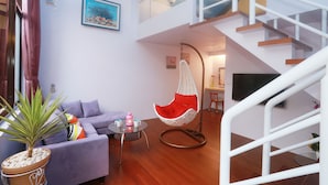 A modern living room with a purple sofa, a hanging chair, a small table, and a staircase. - Zhen Shan Zhuang B&B (Yuanshan)
