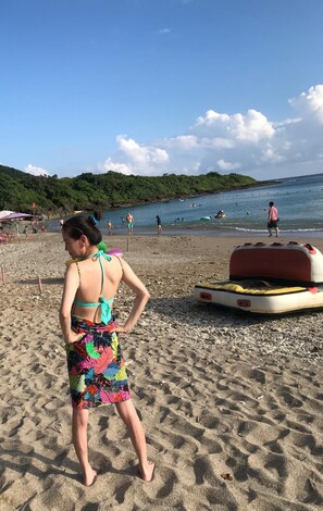 Une plage où l’on voit une personne portant un maillot de bain coloré, une tour de surveillance des sauveteurs et une mer calme.