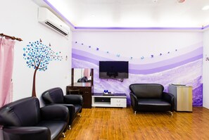 A room with a flat-screen TV mounted on the wall, two leather sofas, a wooden cabinet, and a wall mural with a tree and butterflies. - Kstar 888 Bed and Breakfast (Hengchun)