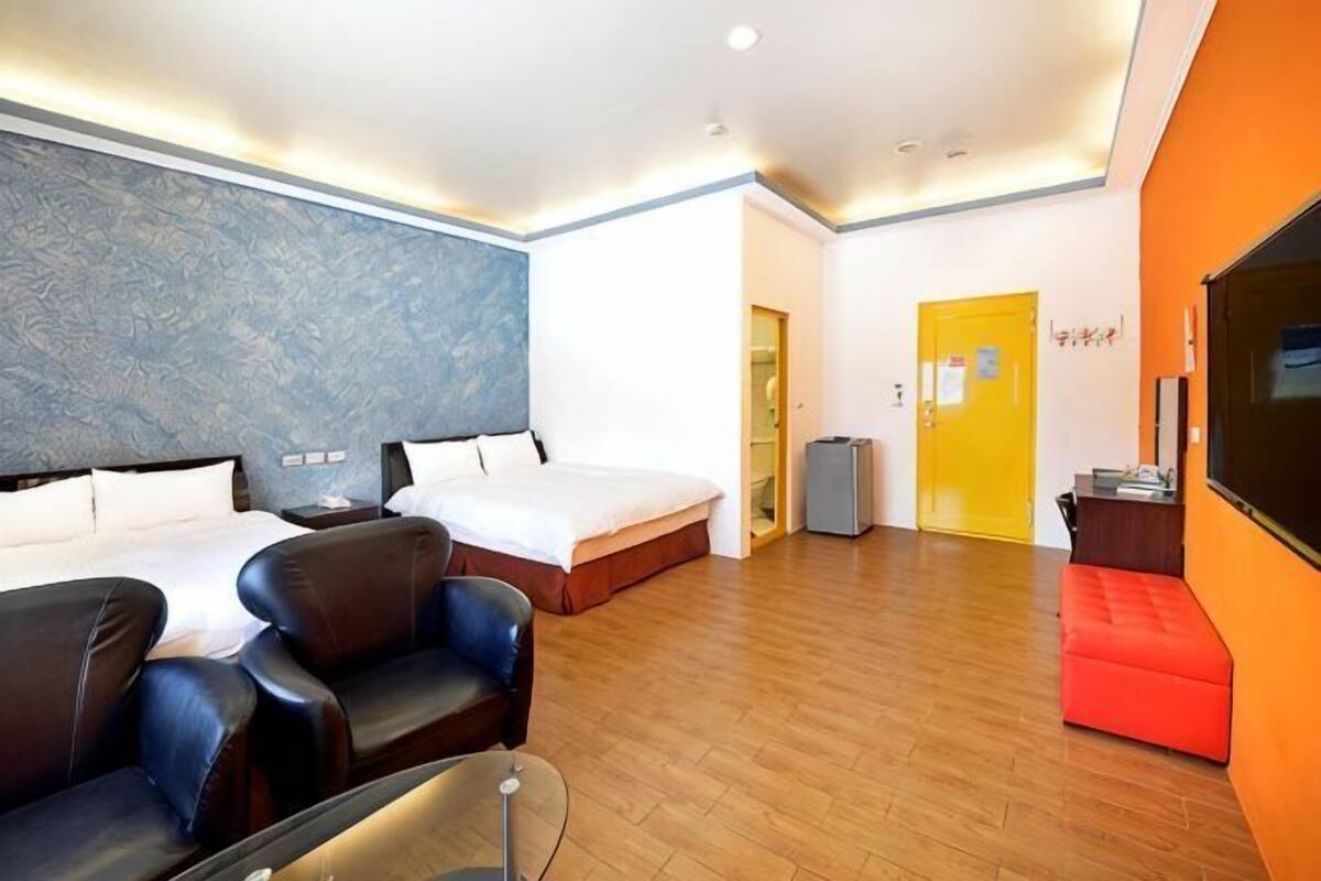 A hotel room with two beds, a TV, a desk, and a red sofa.