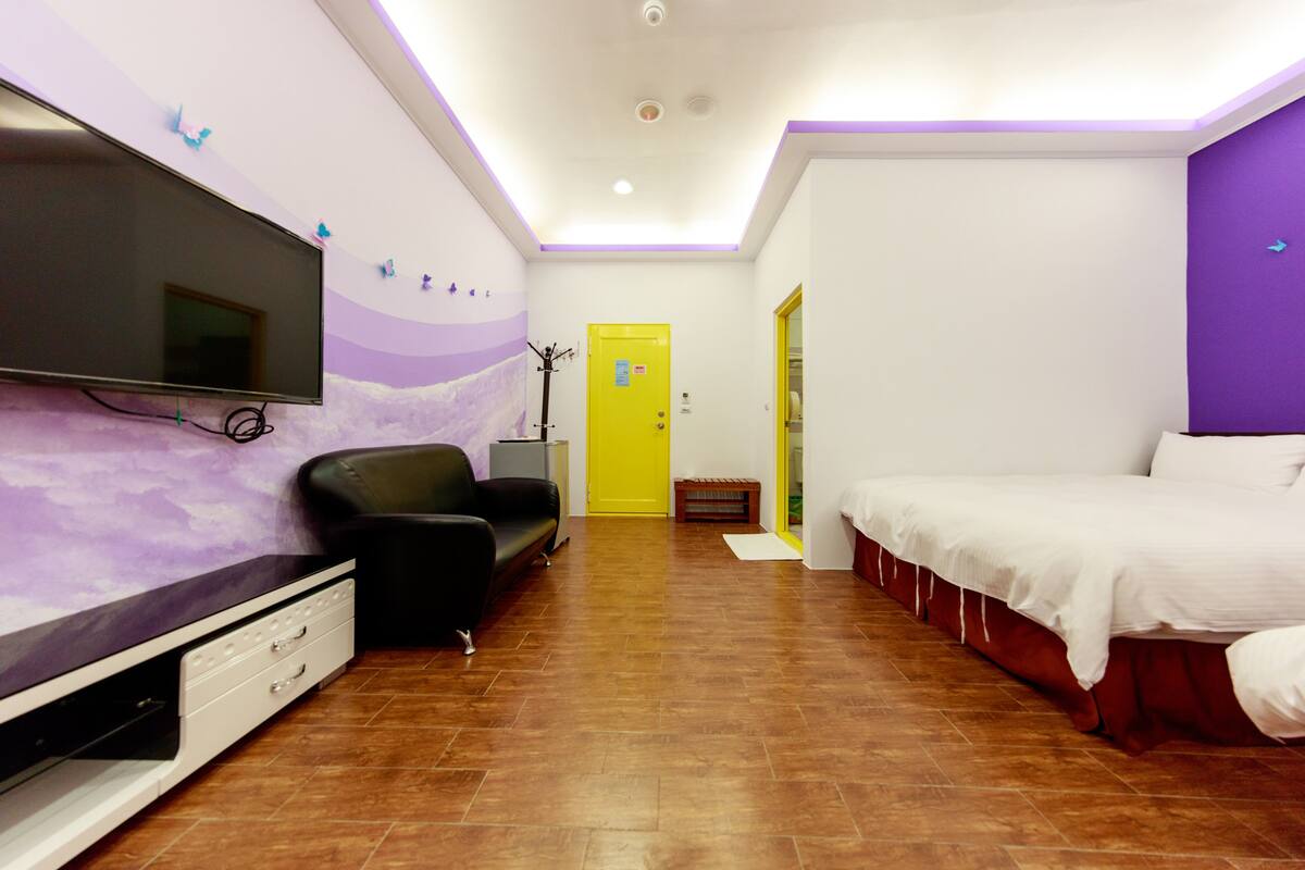 A hotel room with a flat-screen TV, a sofa, a bed, and a door leading to another room.