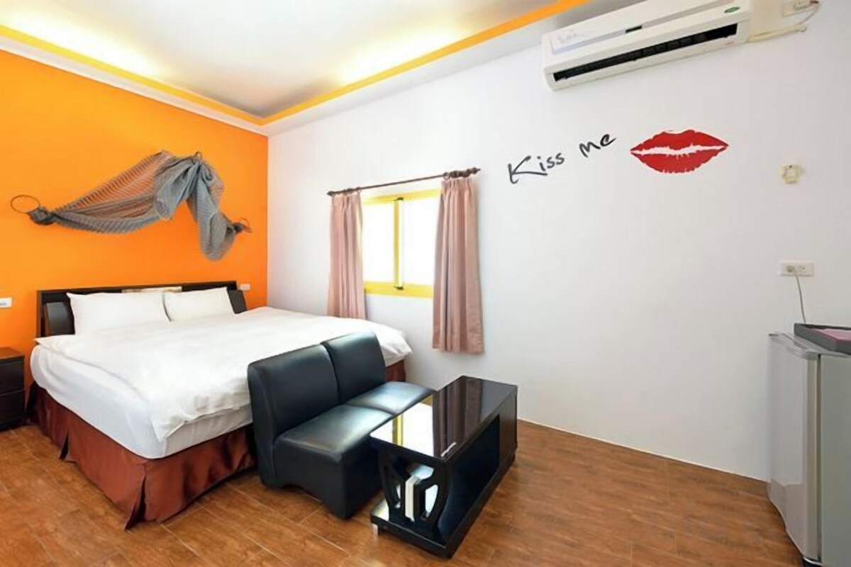 Une chambre d’hôtel avec un lit, un bureau, un hamac et un mur orné d’un autocollant sur lequel on peut lire « Embrasse-moi ».