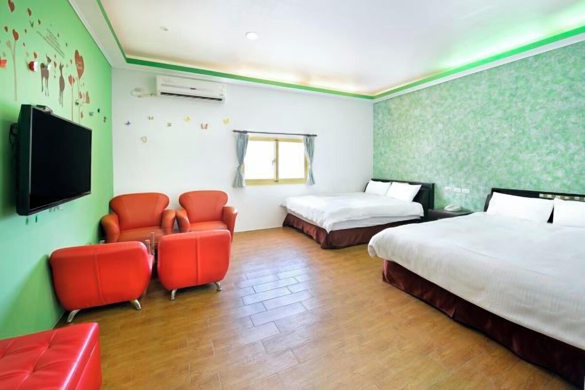 A hotel room with two beds, a TV, a window, and a green wall.