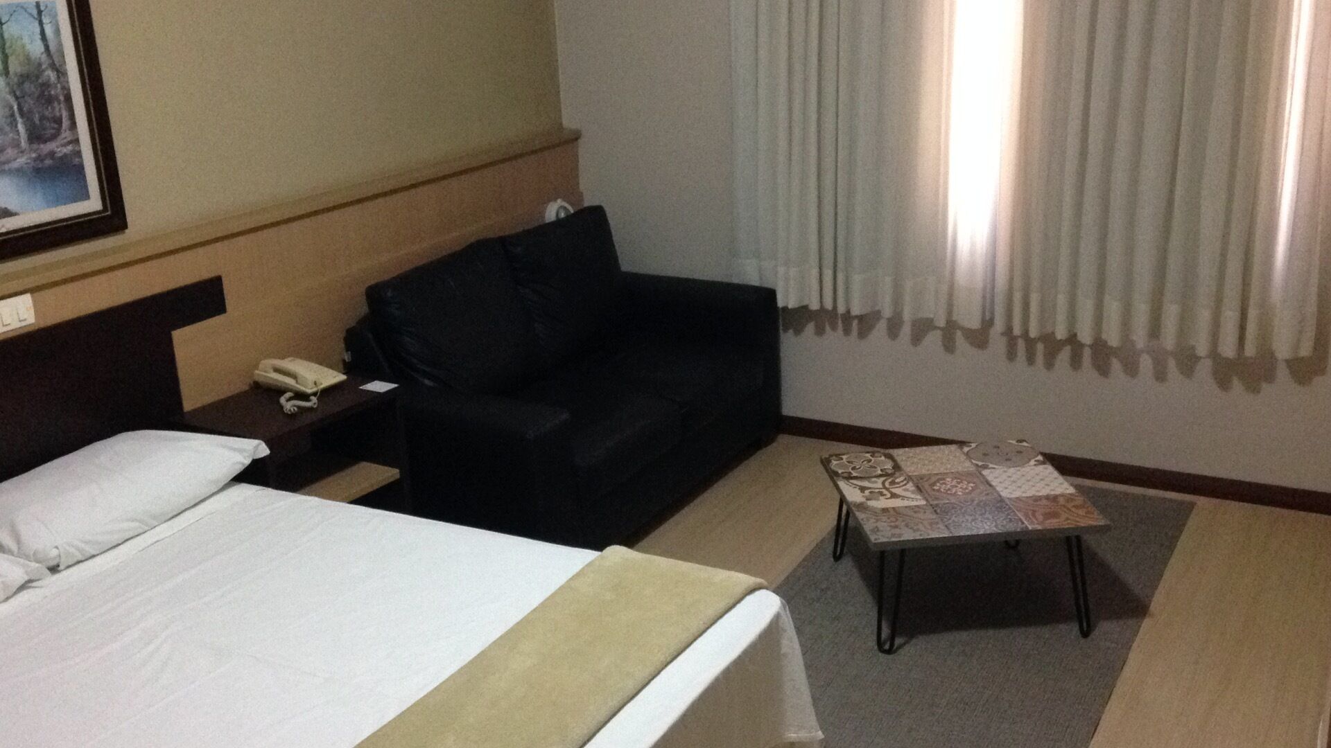 A hotel room with a bed, a black sofa, a small table, and a painting on the wall.