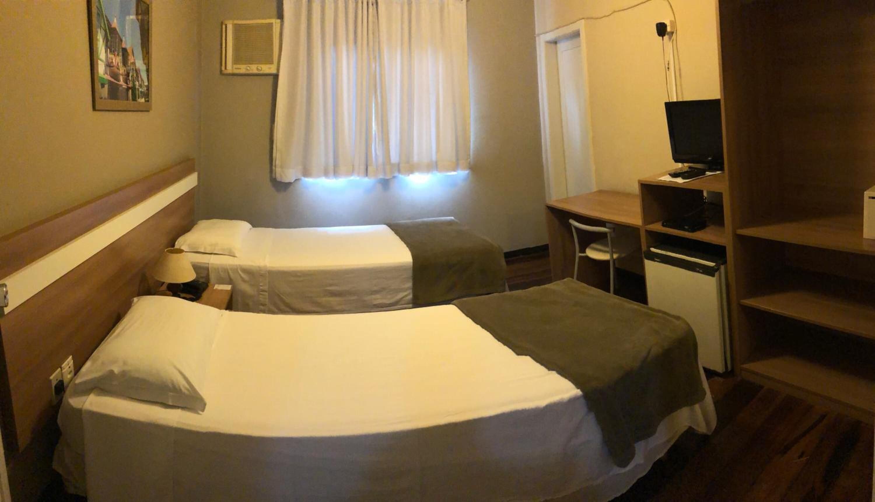Habitación de hotel con dos camas individuales, un escritorio con silla, un televisor y un mueble auxiliar.