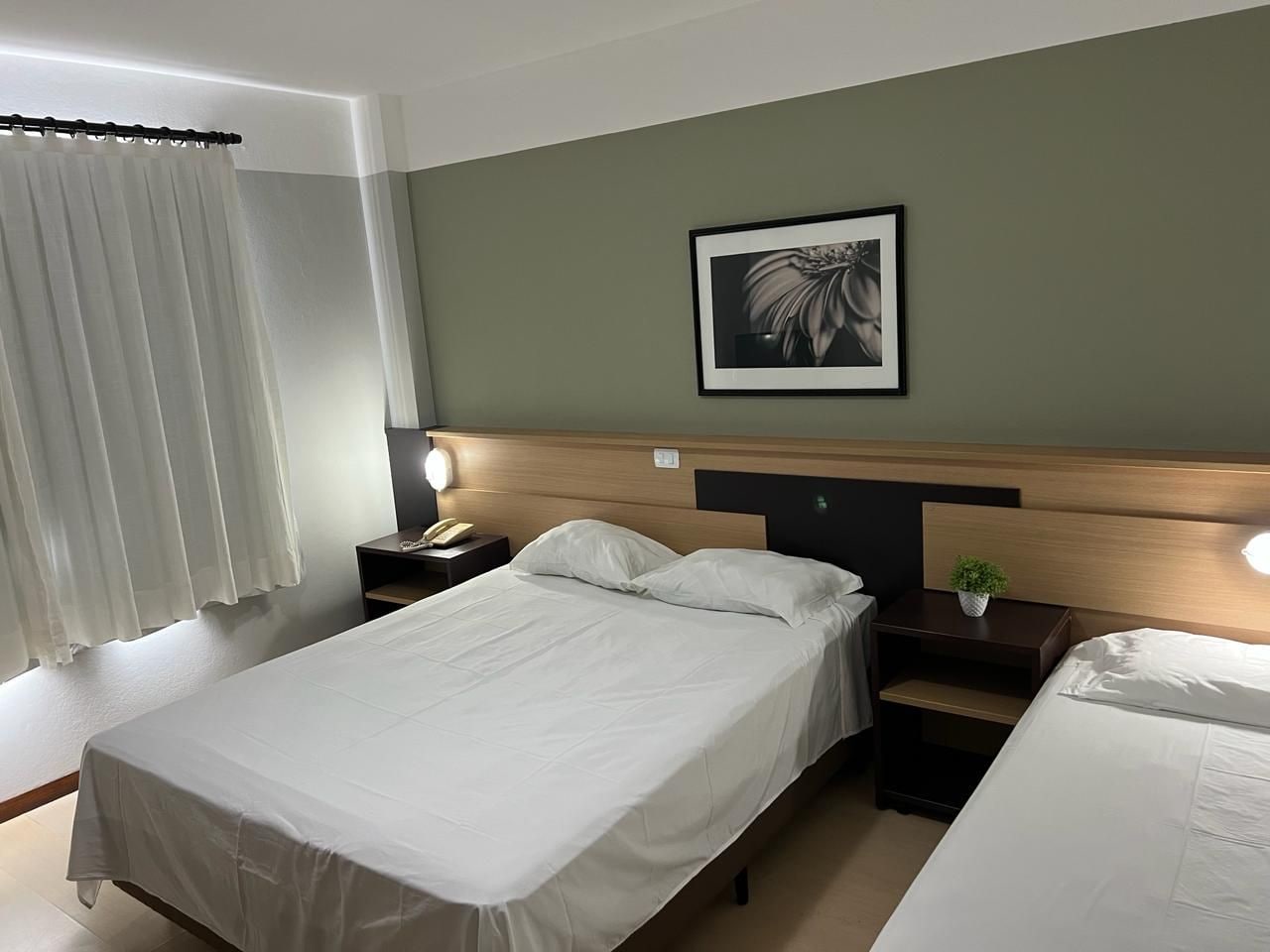Una habitación de hotel con una cama, mesitas de noche, una lámpara, un cuadro en la pared y una ventana con cortinas.