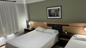 Una habitación de hotel con una cama, mesitas de noche, una lámpara, un cuadro en la pared y una ventana con cortinas.