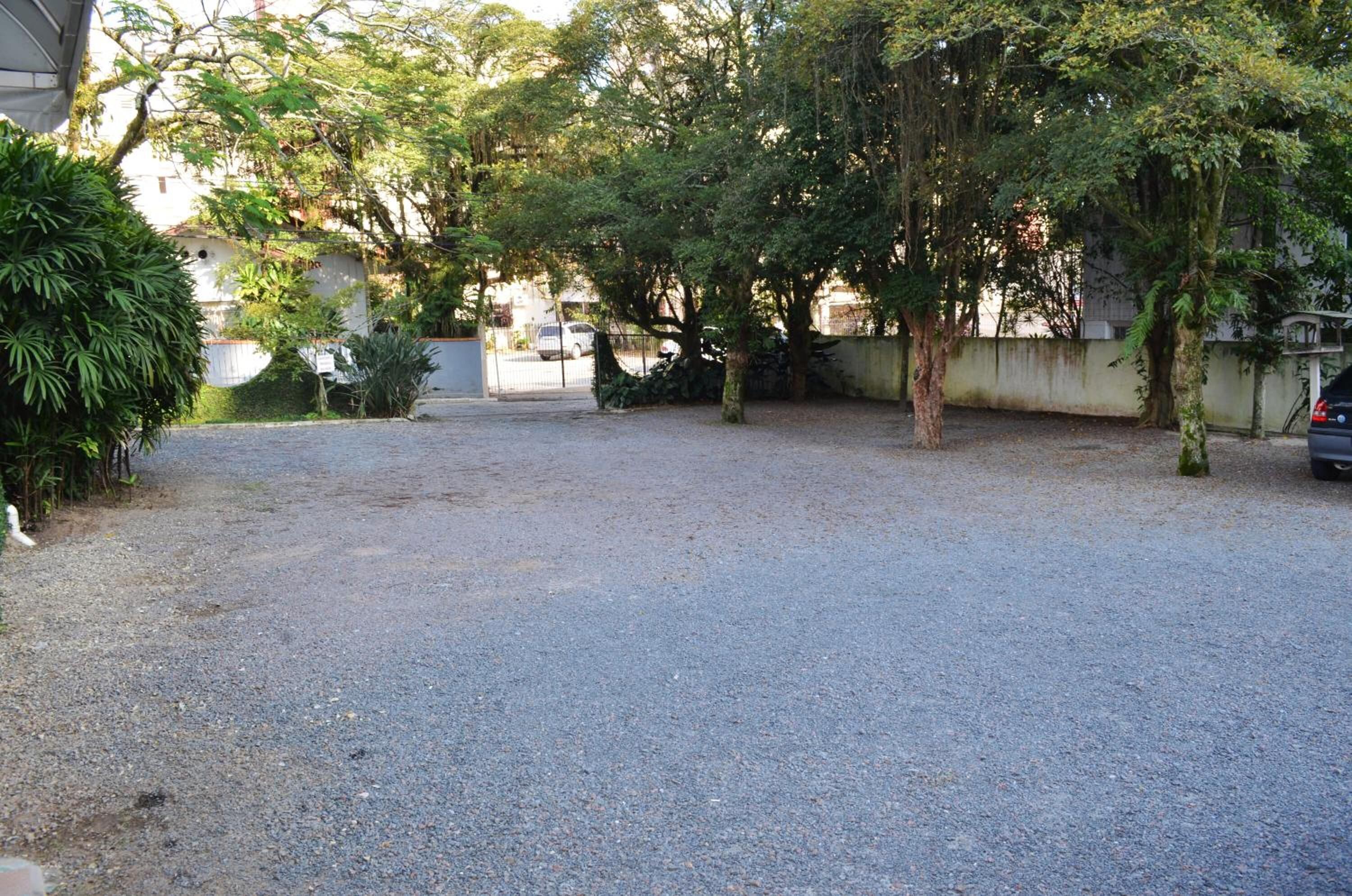 A gravel driveway leading to a gated entrance with trees and a parked car.