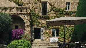 Un edificio de piedra con muros cubiertos de hiedra, una entrada en arco y mobiliario exterior con mesa y sillas.