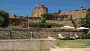 Un castillo con foso y piscina con sillas de descanso.