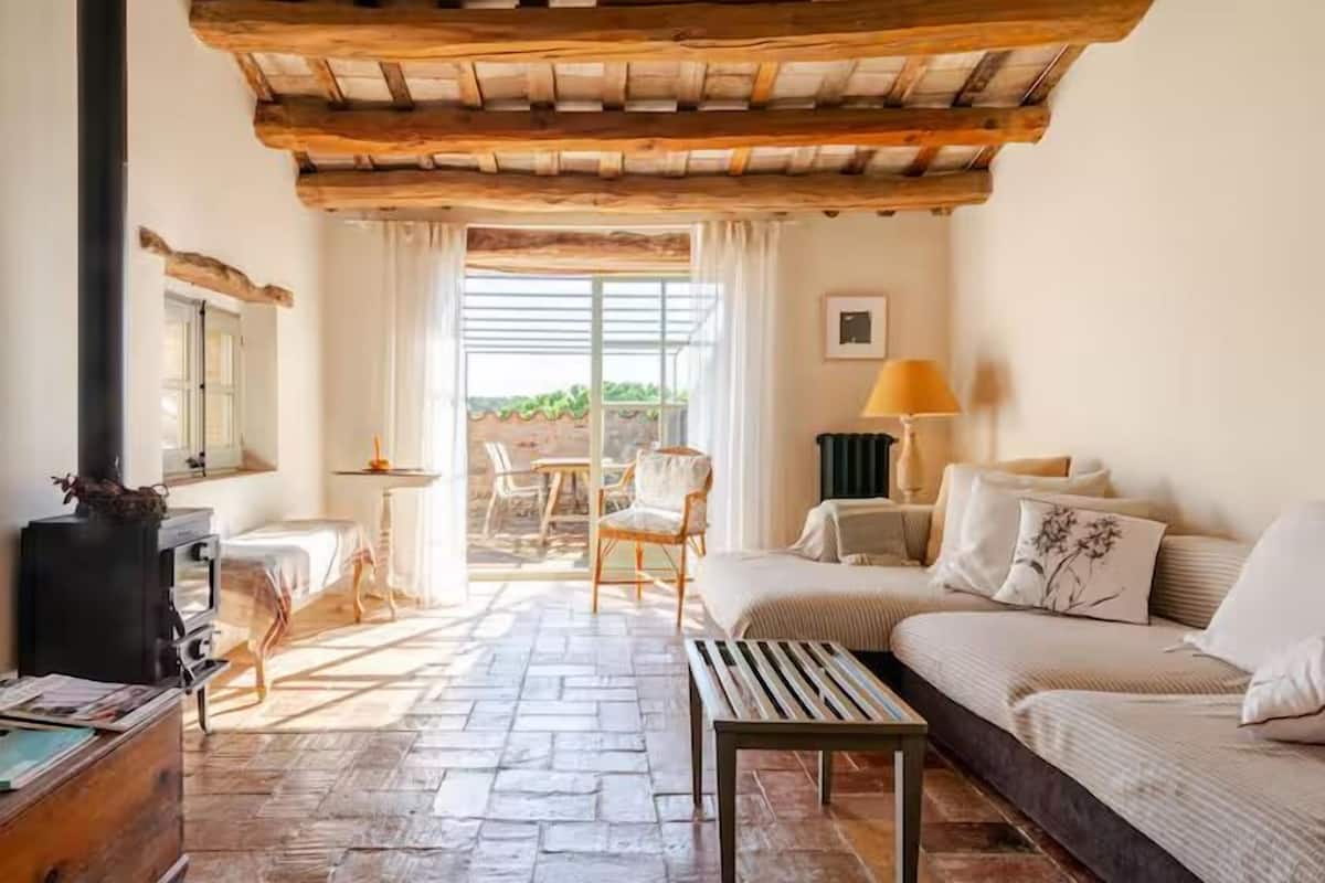 A cozy room with a stone floor, a sofa, a small table, a lamp, and a fireplace.