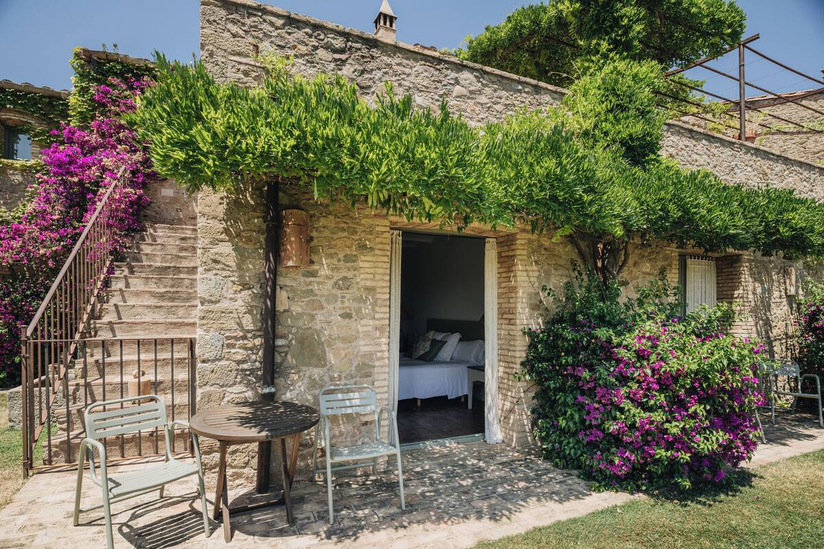 A stone building with a bed, a table, and chairs outside.