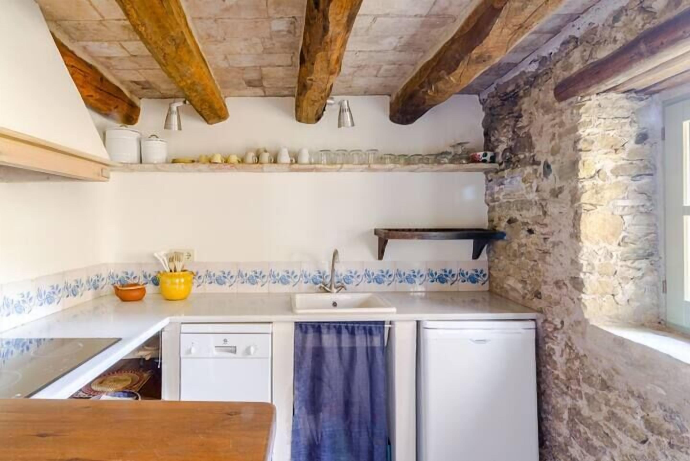 Una cocina rústica con vigas de madera a la vista, pared de piedra y salpicadero de azulejos.