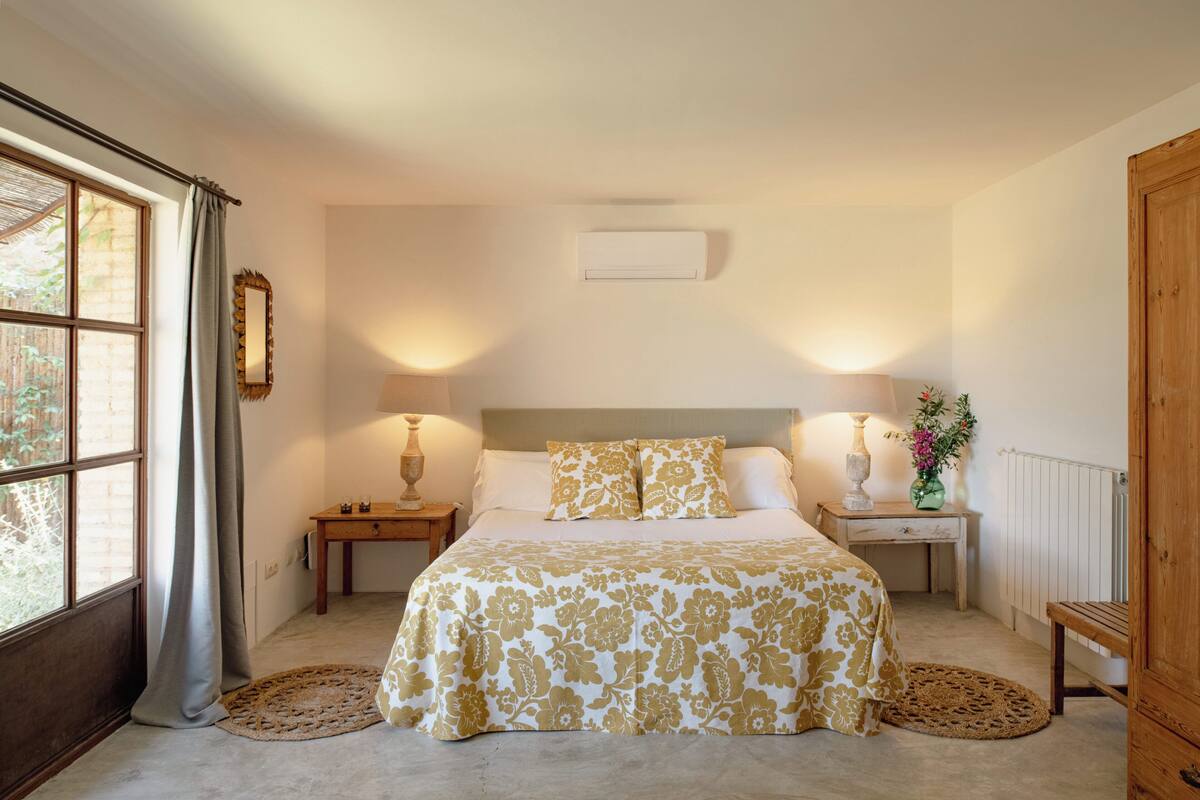A bedroom with a bed, two bedside tables, a nightstand, a mirror, and a window with curtains.