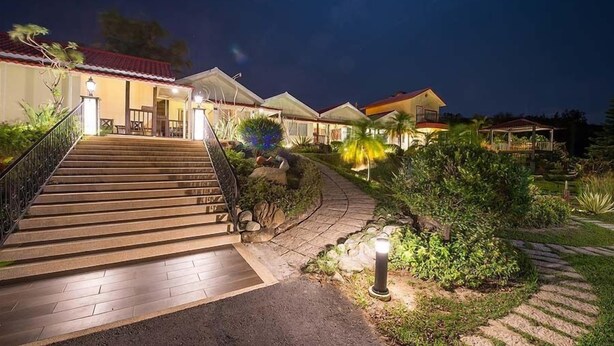 A well-lit hotel entrance with a staircase leading to the main building, surrounded by landscaped gardens and outdoor seating areas. - Red Sun (Checheng)