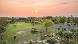 A landscaped garden with a small building, a paved area, and a view of the ocean at sunset. - Red Sun (Checheng)