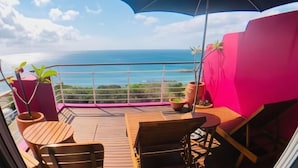 Un balcon doté de meubles en bois, d’un grand parasol et offrant une vue sur l’océan.