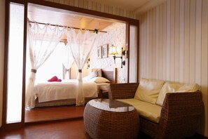 Een kamer met een bed, een rieten bank, een kleine tafel en een wandlamp.
