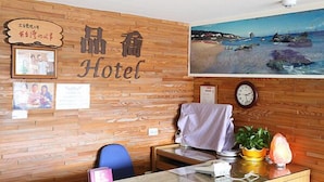 Un hall d'hôtel avec des panneaux de bois, un comptoir d'accueil, une horloge et un tableau représentant une scène de plage.