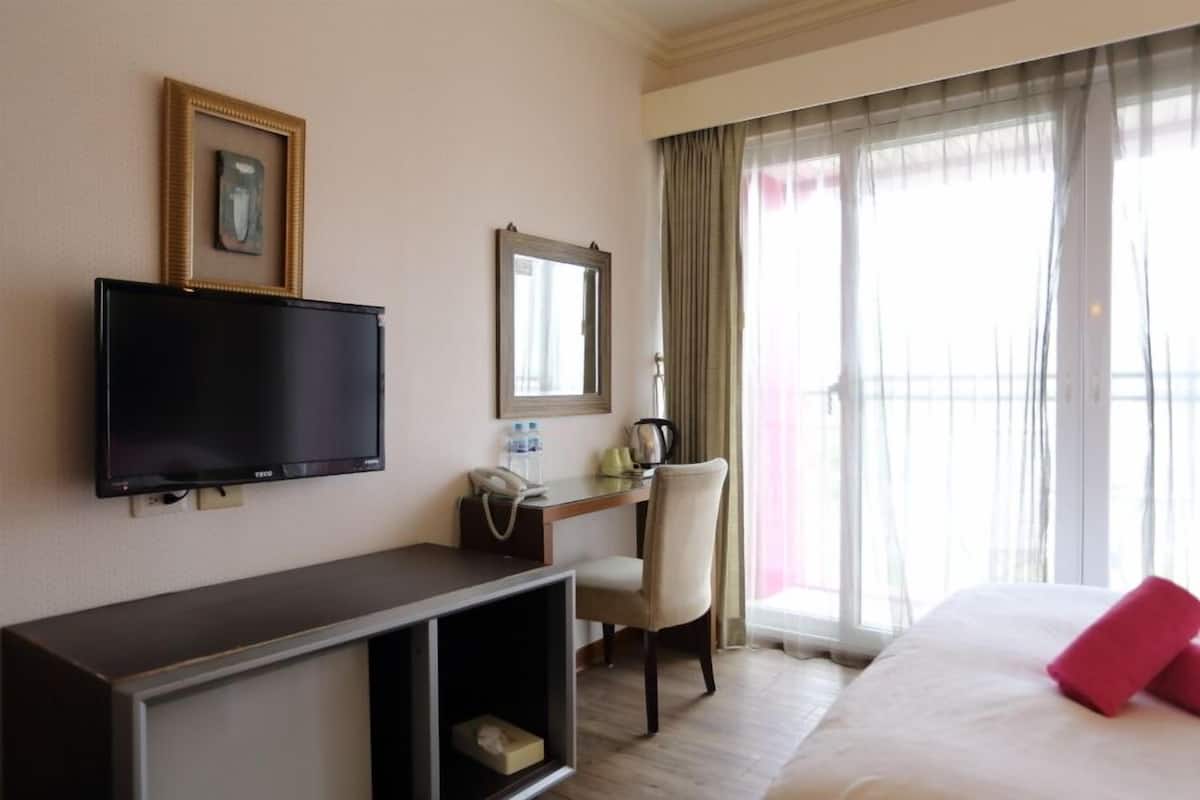 A hotel room with a bed, a desk with a chair, a television, and a window with curtains.