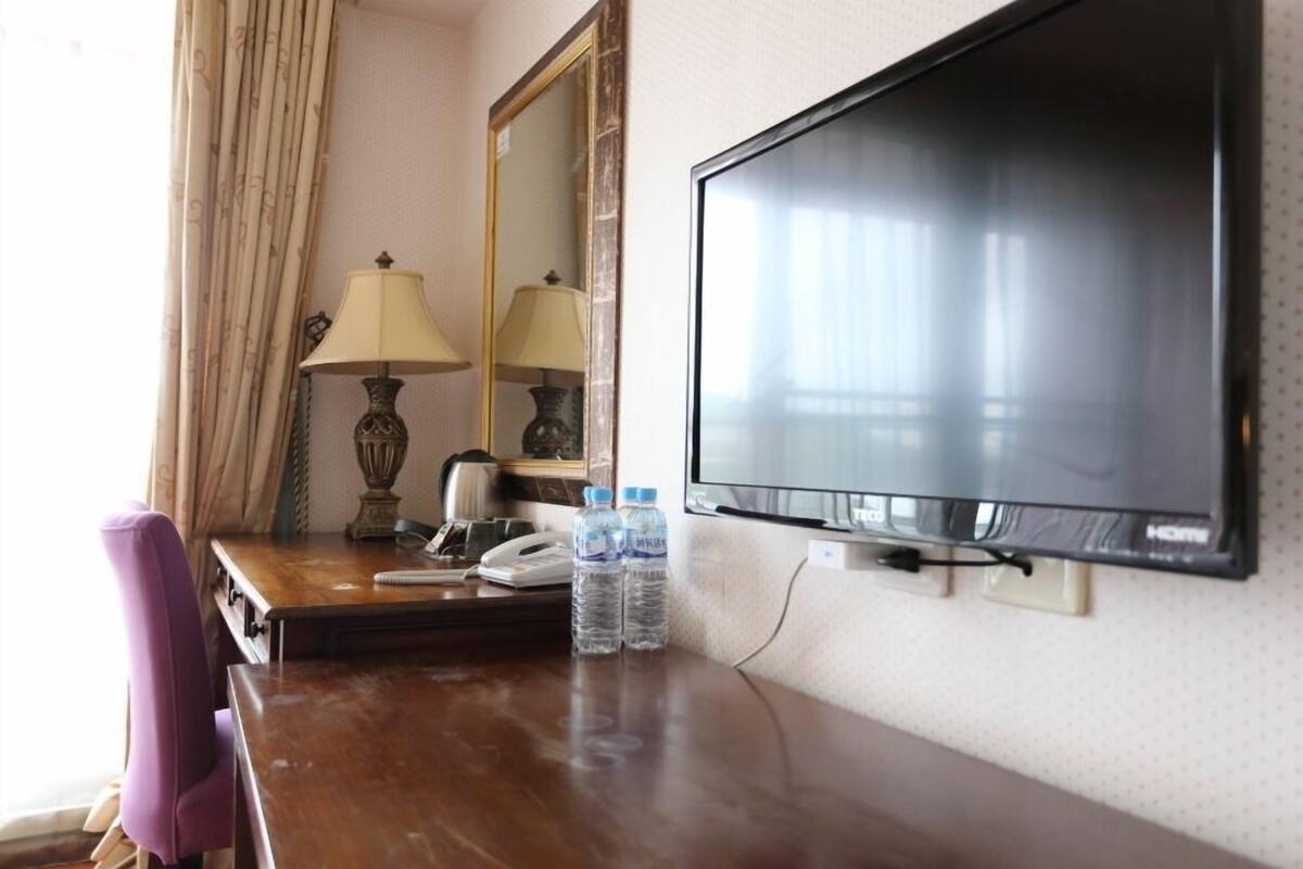 A hotel room with a wooden desk, two lamps, a flat-screen TV, a mirror, and a purple chair.