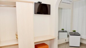 Una habitación de hotel con armario, televisión de pantalla plana, refrigerador pequeño y espejo.