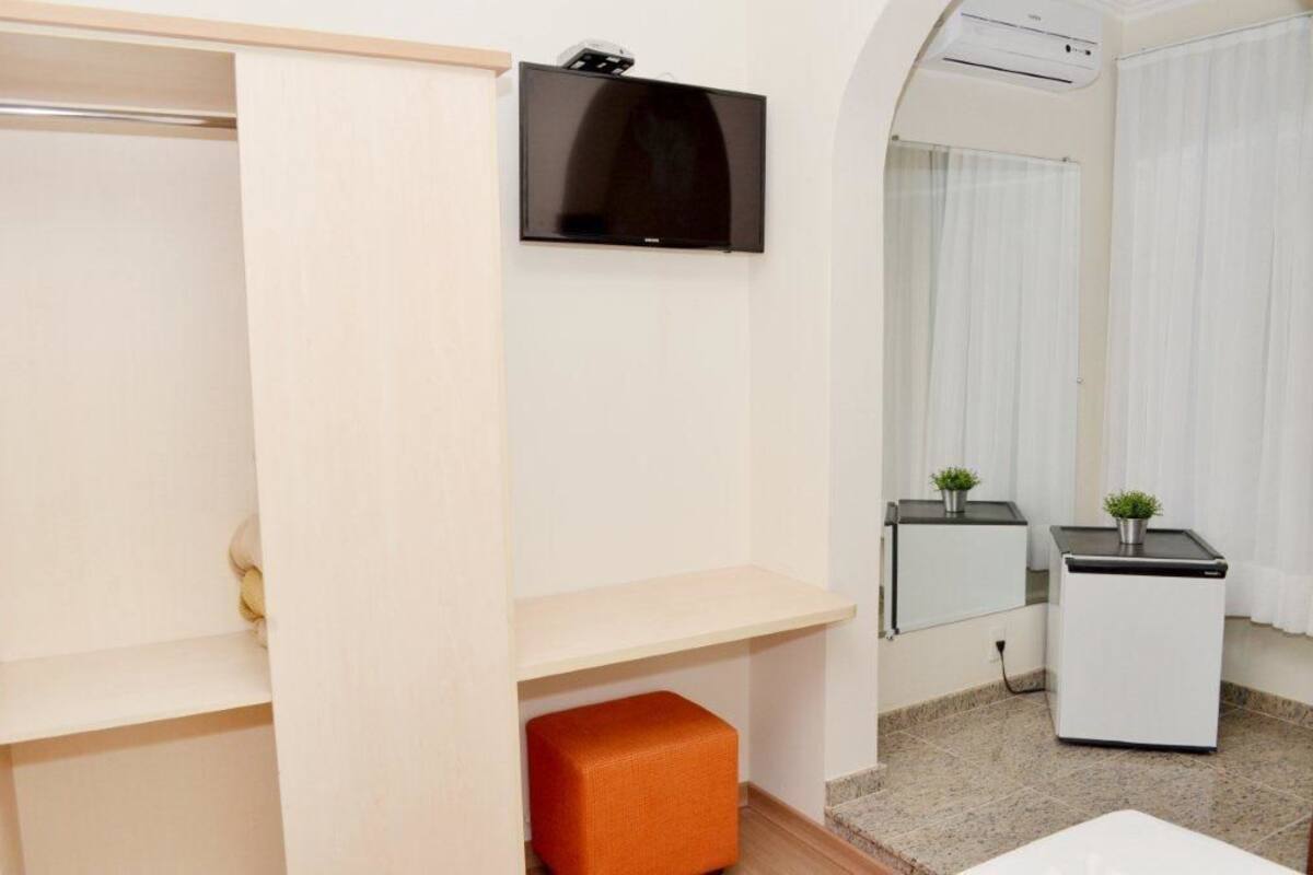 Una habitación de hotel con armario, televisión de pantalla plana, refrigerador pequeño y espejo.