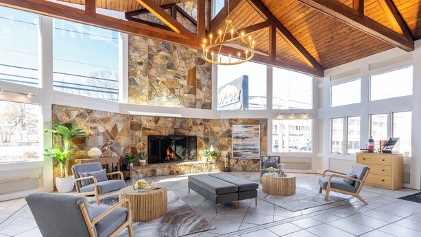 A spacious lobby with a stone fireplace, modern seating, large windows, and a high ceiling. - Sea View Inn (Old Orchard Beach)