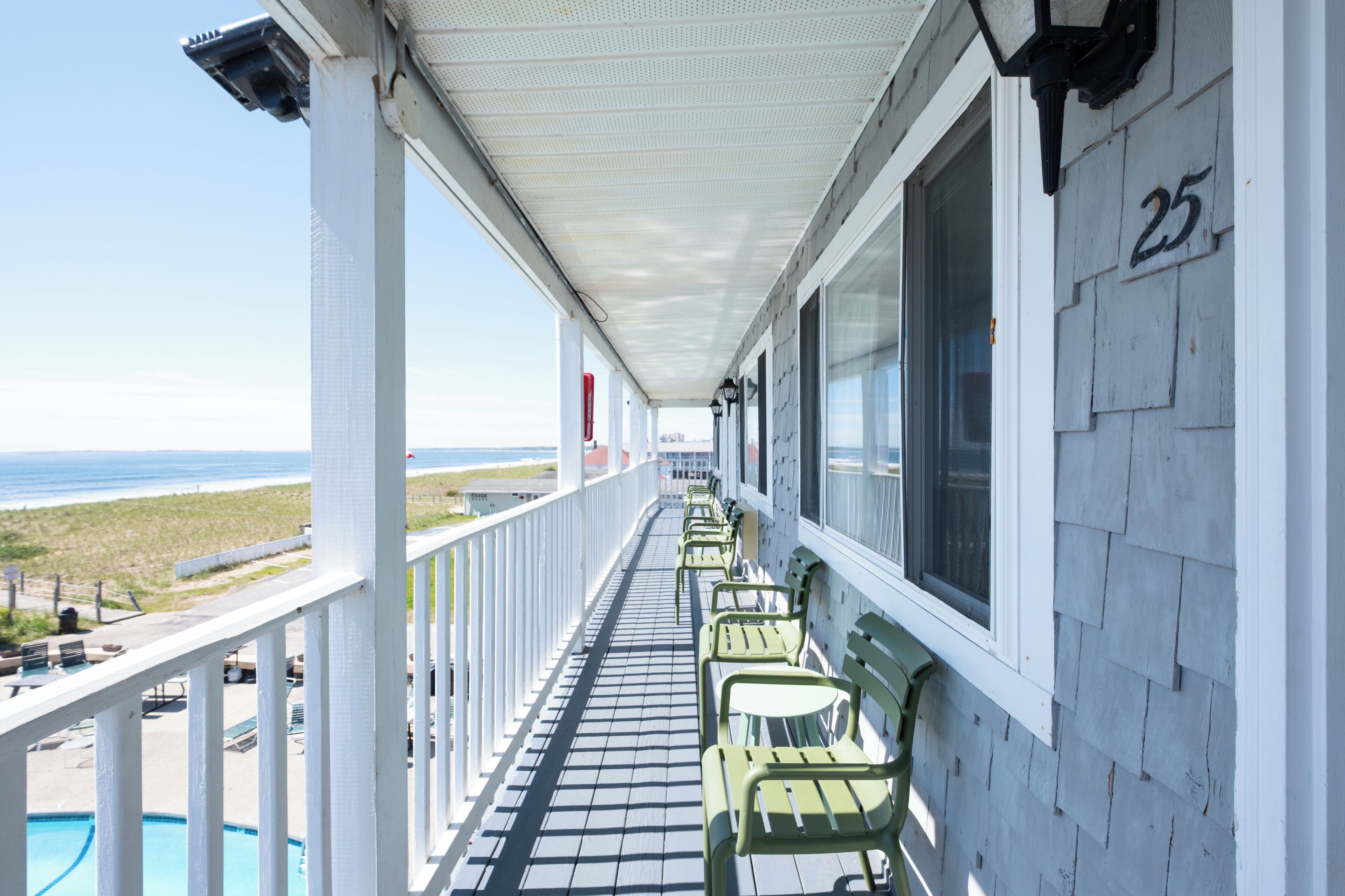 A balcony with a view of the beach, a pool, and numbered room 25.