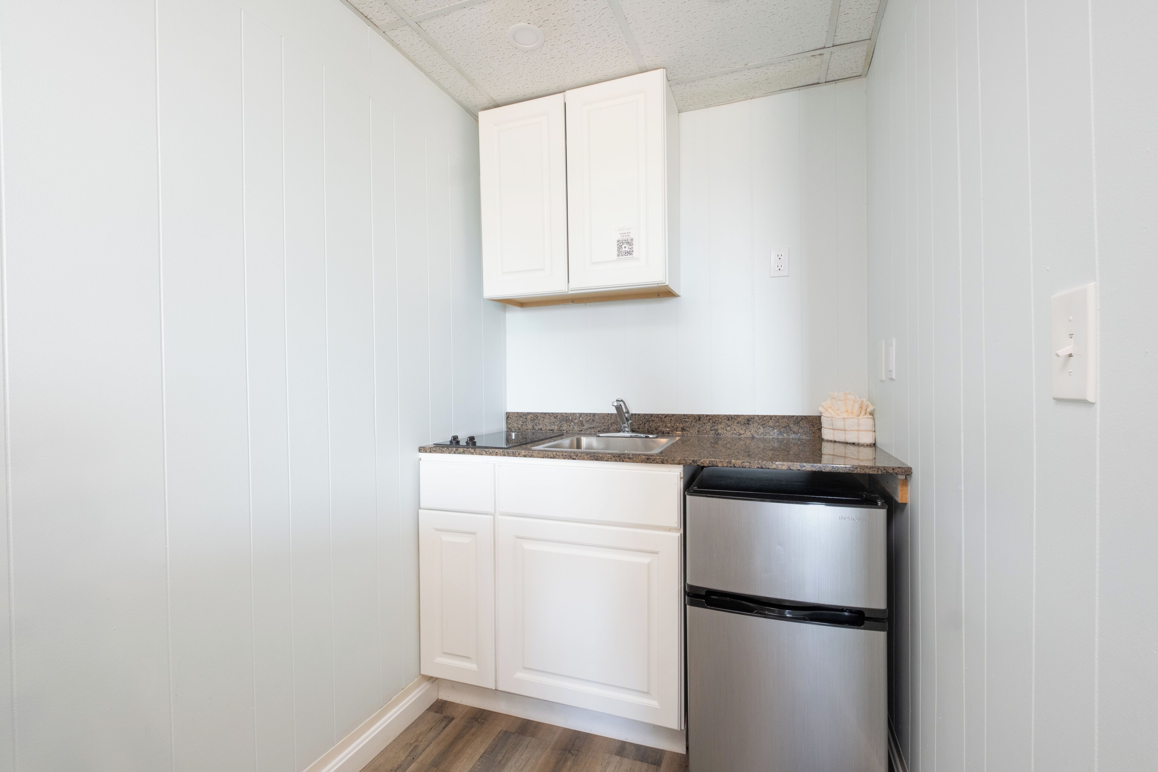 A compact kitchen with white cabinetry, a stainless steel refrigerator, and a granite countertop.