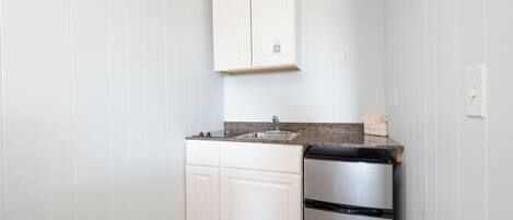 A compact kitchen with white cabinetry, a stainless steel refrigerator, and a granite countertop.