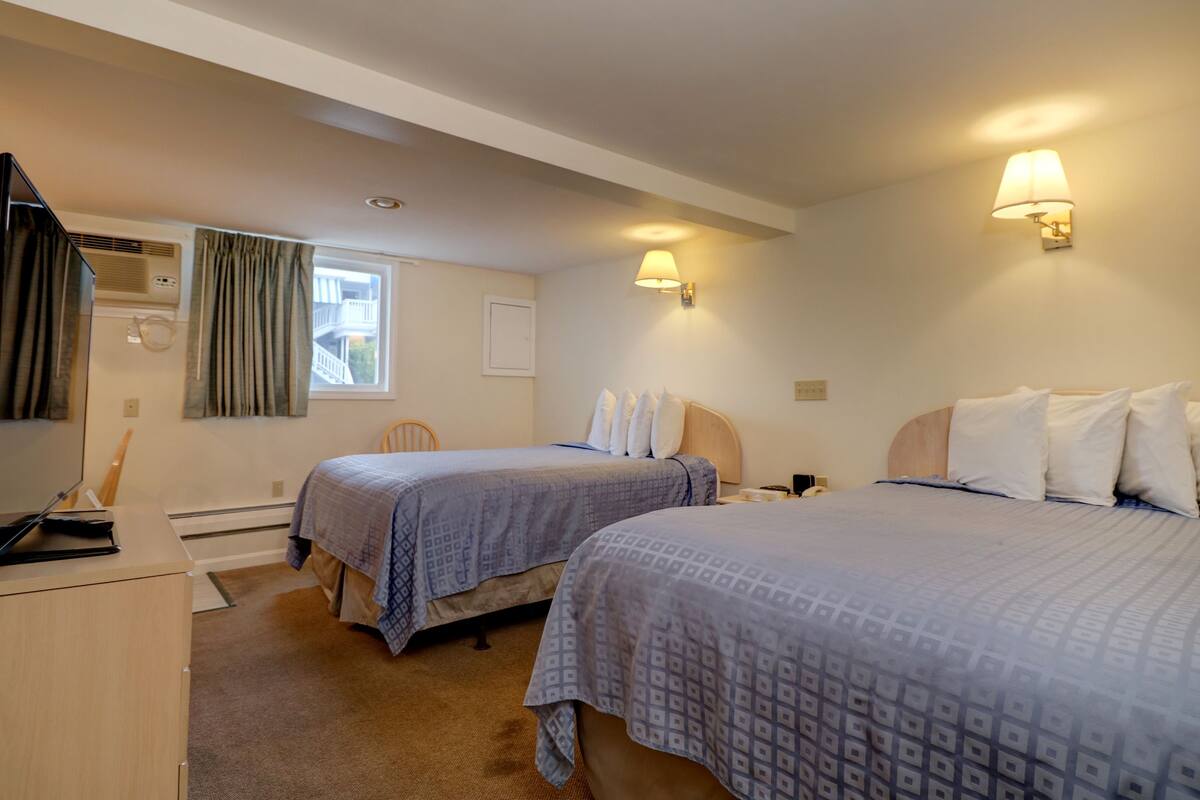 A hotel room with two beds, a desk, a chair, and a window with curtains.