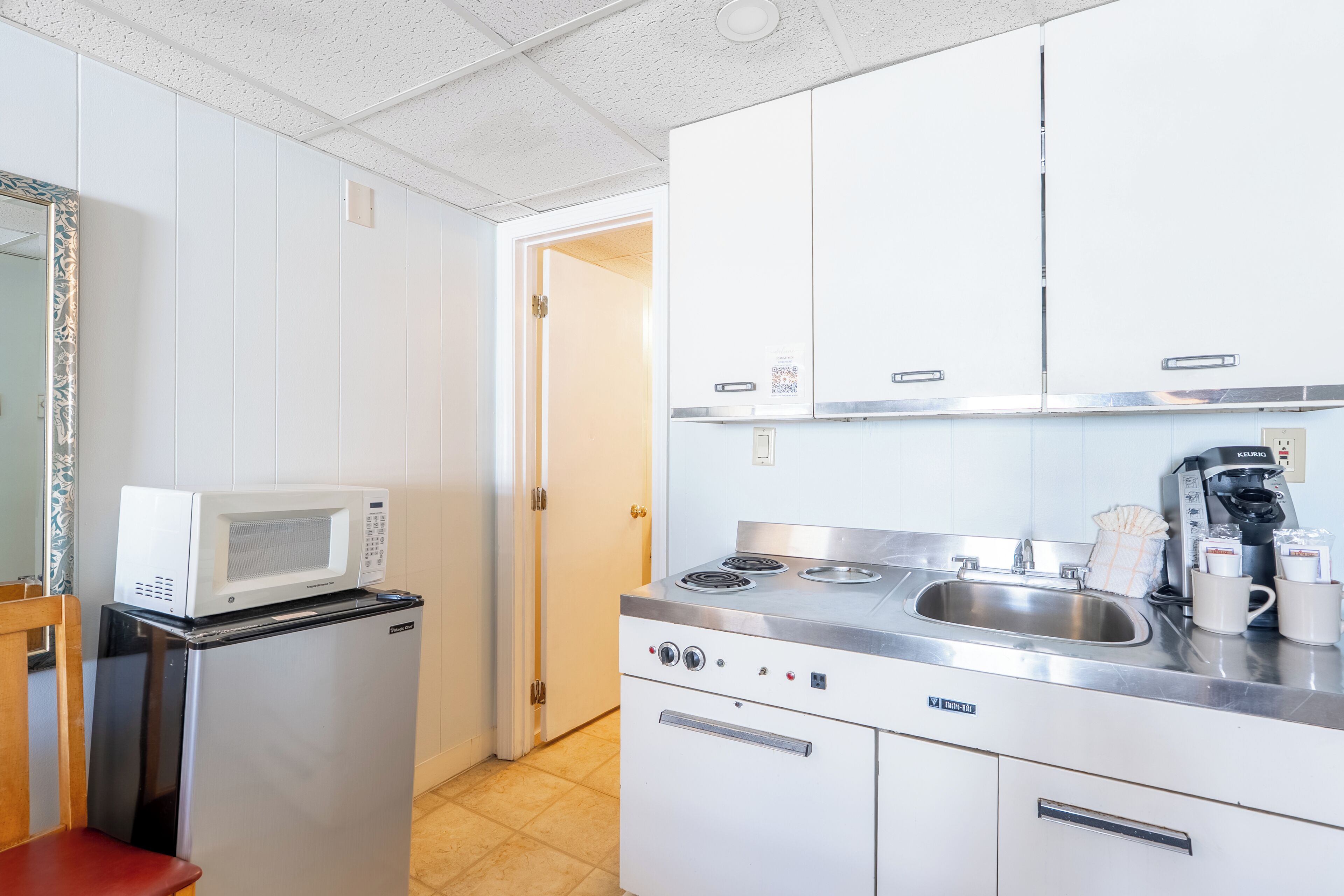 A compact kitchen with a microwave, refrigerator, stove, sink, and coffee maker.