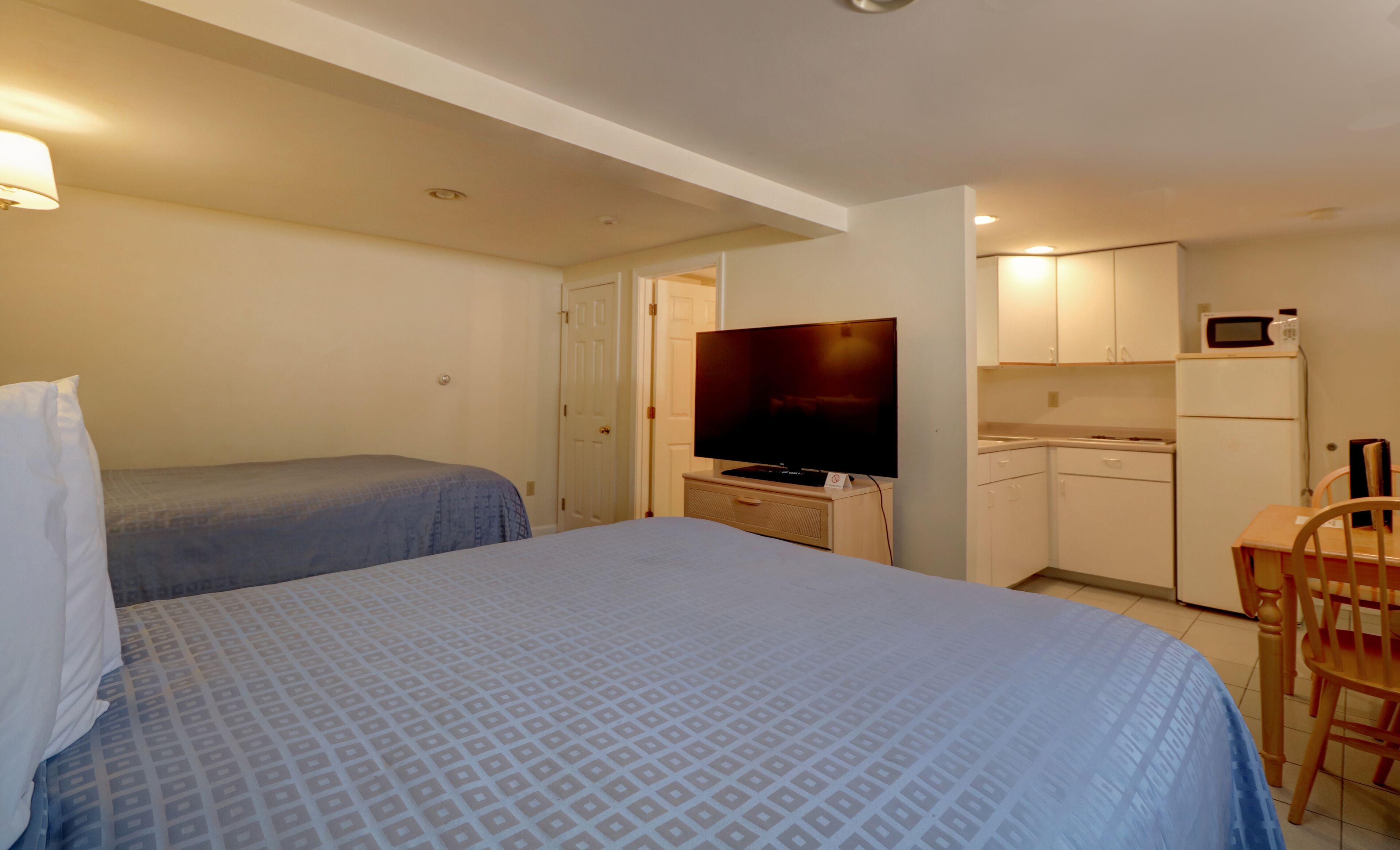 A bedroom with two beds, a television, a kitchenette, and a dining area.
