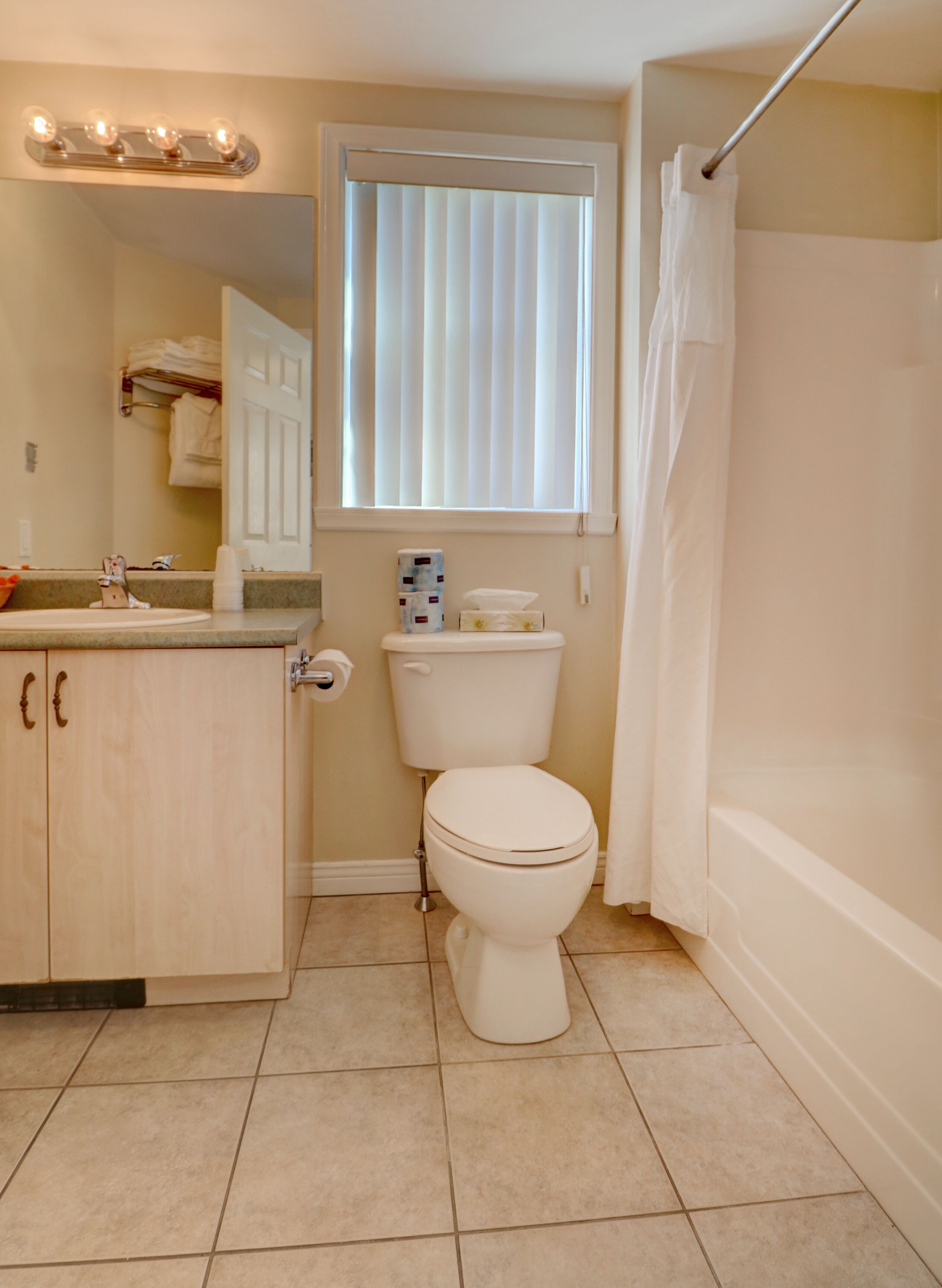 A bathroom with a toilet, sink, vanity, and a window with blinds.