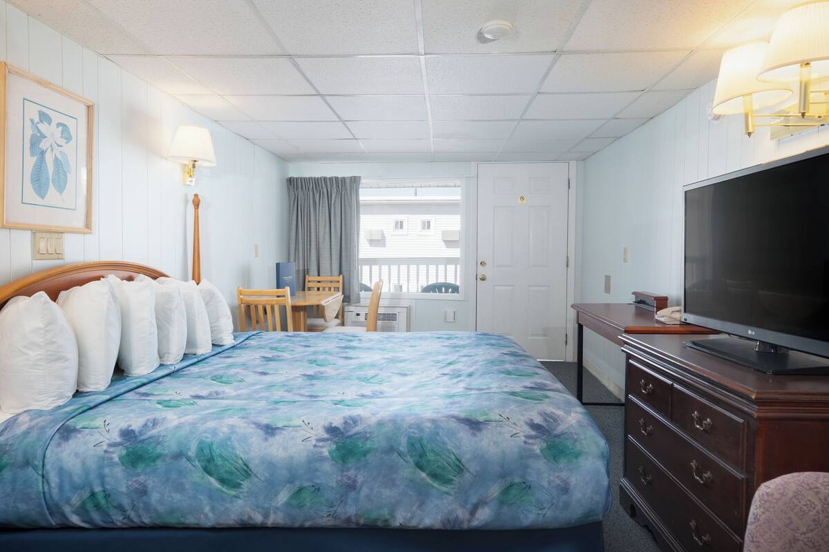 A hotel room with a large bed, a television, a desk, and a chair.