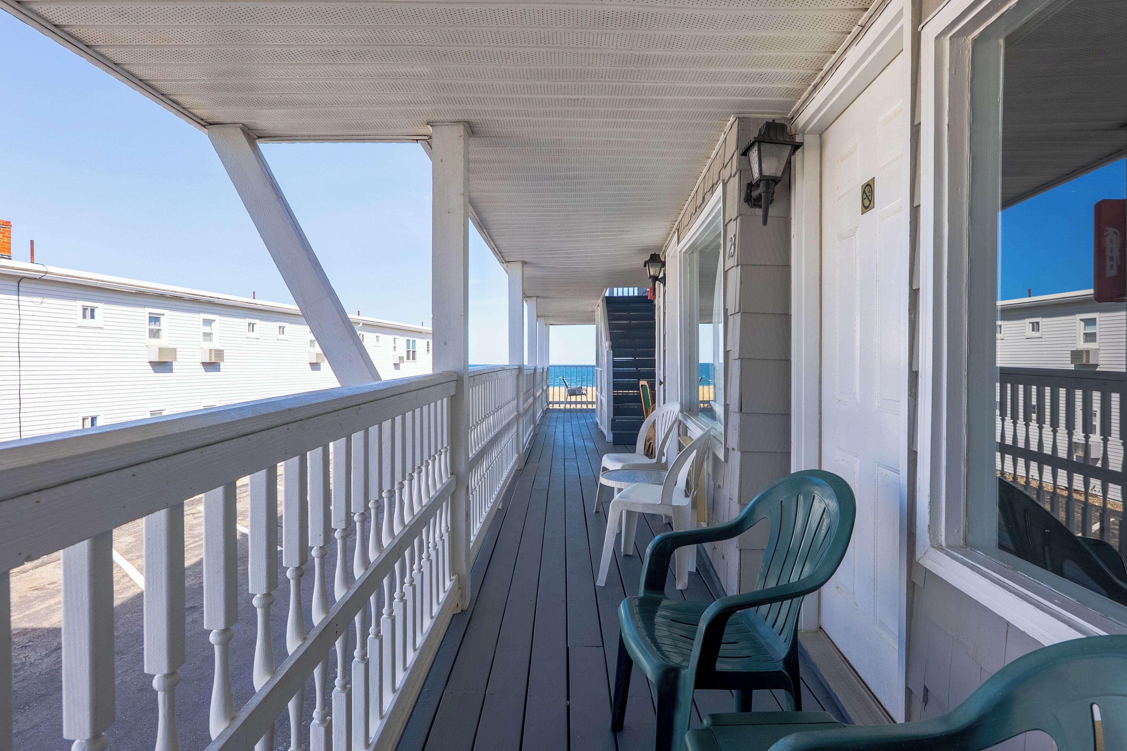 A covered balcony with white railings, a small table, and two green chairs.