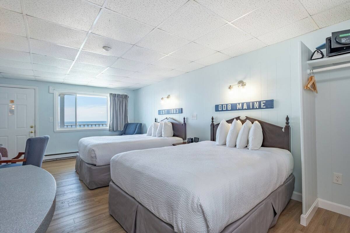 A hotel room with two beds, a window with a view, a desk, and a chair.