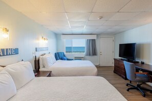 A hotel room with two beds, a TV, a desk, and a view of the ocean.