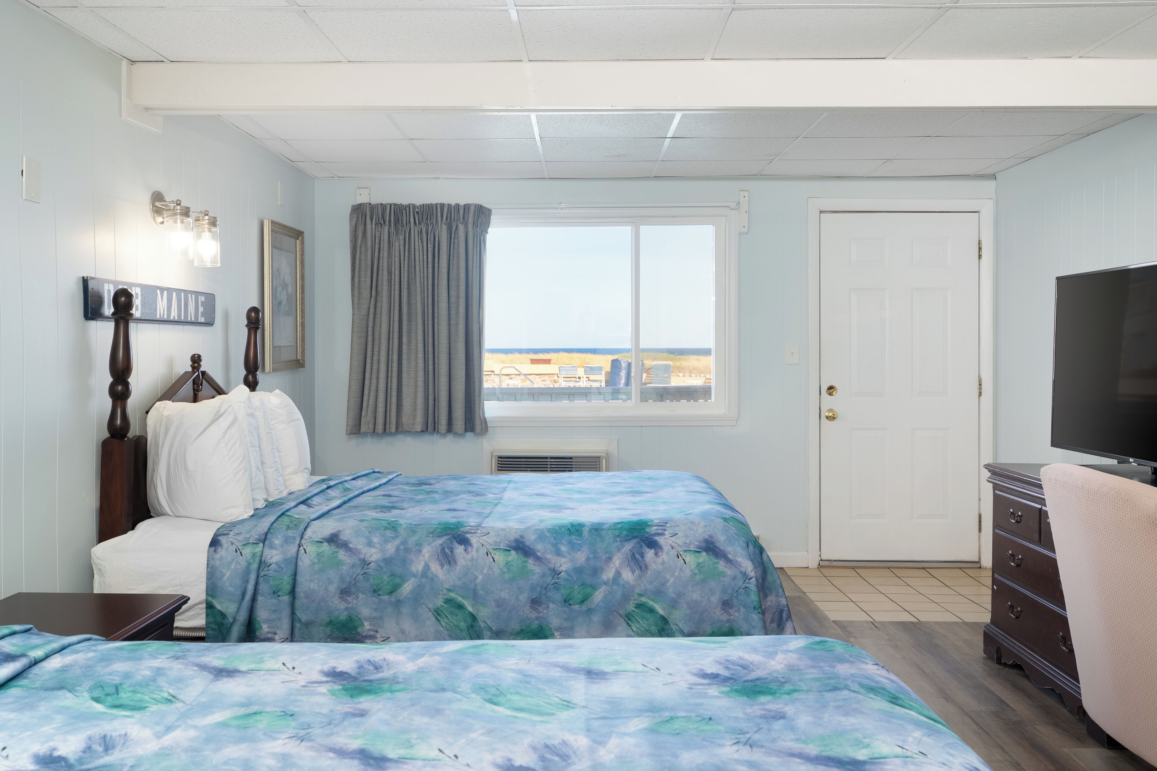 A bedroom with a bed, a chair, a dresser, a television, a window with a view, and a sign on the wall.