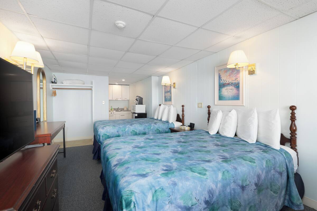 A hotel room with two beds, a TV, a dresser, and a bathroom visible in the background.