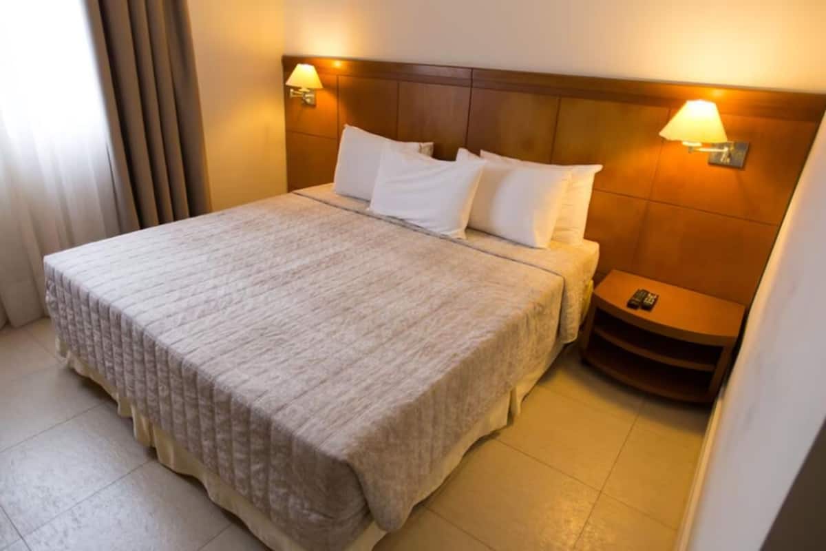 Een hotelkamer met een groot bed, twee bedlampen, een nachtkastje en een telefoon op het nachtkastje.