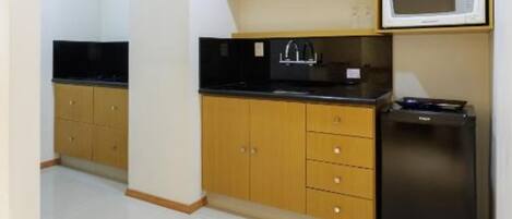 A compact kitchen with wooden cabinets, a black countertop, a microwave, and a refrigerator.