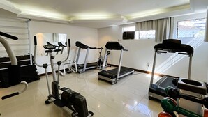 Une salle de sport moderne, équipée de tapis de course, d’un appareil elliptique et de poids libres.