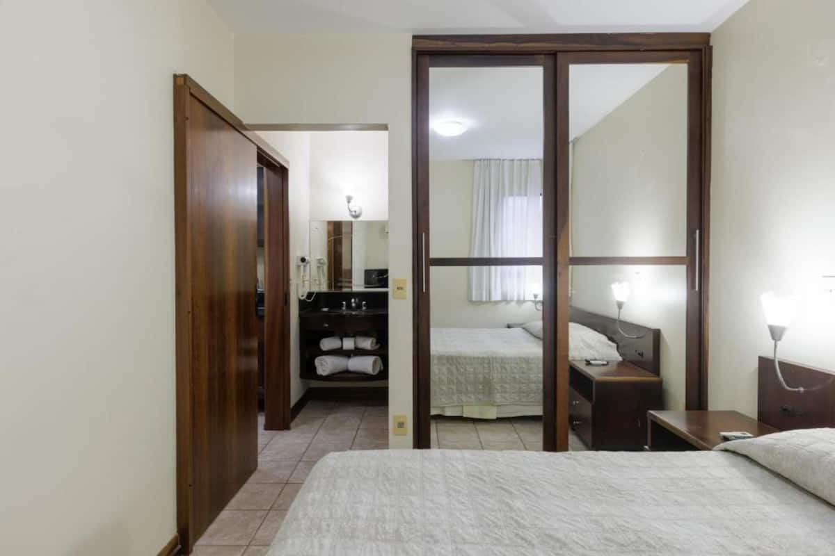 Een hotelkamer met een bed, een bureau, een kledingkast en een badkamer die door een geopende deur zichtbaar is.